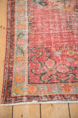 Distressed raspberry red Oushak runner shows worn pile texture and turquoise floral border.