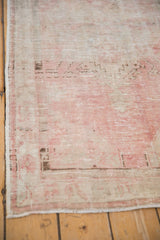 Worn corner of a vintage Oushak runner with low-pile texture in soft pink and brown.