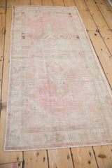 Long perspective view of a vintage Oushak runner with a heavily worn pink and silver design.