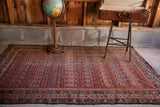 Antique Persian Malayer tribal rug corner featuring cranberry and blue patterns, visible wear.