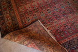Hand-knotted foundation and worn pile on an antique Malayer rug's cranberry tribal pattern.