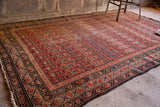 Antique Persian Malayer rug, tribal field, geometric border, and aged cranberry tones.