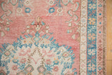 Distressed Oushak rug pile with blush, ivory floral bouquet, and blue border.