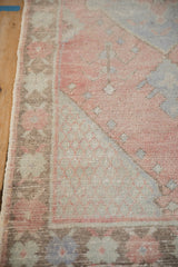 Distressed Oushak rug corner with visible knot heads and faded pink, pale blue patterns.