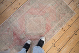 Distressed vintage Oushak rug with serrated diamond motif, soft raspberry red, and visible wear.
