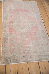 Distressed Oushak rug corner, faded raspberry, ivory, platinum tones with visible wear.