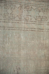A distressed Oushak's low-pile texture, showing even wear and a pale geometric border.