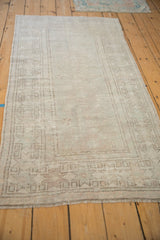 Angled view of a distressed Oushak rug with a tone-on-tone geometric border in soft silver hues.