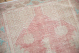 Distressed vintage Oushak rug pile showing soft raspberry red, ivory, and pale green hues.