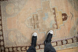Feet on vintage distressed Oushak rug, highlighting heavy abrashes and soft, muted palette.