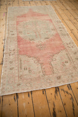 Distressed vintage Oushak rug corner showing blush, seafoam, brown floral motifs and even wear.