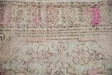 Detailed texture of a distressed vintage rug with worn knot heads and bright fuchsia floral accents.