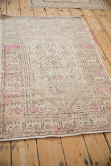 Angled view of a distressed vintage rug showing its primitive floral border and low-pile texture.