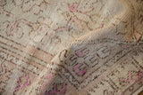Folded corner of a distressed Oushak rug highlights its low pile and hand-knotted texture.
