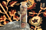 A rolled antique Kerman rug fragment in a glass bottle showing its woven foundation.