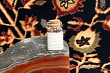 Tiny souvenir bottle with cork holding a colorful antique Kerman rug fragment.