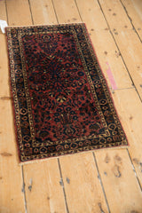Angled view of an antique Sarouk mat highlighting the deep raspberry red and dark sapphire blue floral pattern.