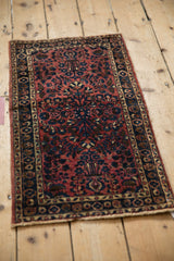 Angled view of the antique Persian Sarouk mat's raspberry red and dark blue field of blossoms.