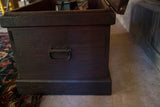Antique wooden cabinet side, dark wood with visible grain and an ornate metal handle.