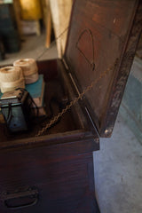 Open antique wooden cabinet top, revealing dark interior, support chain, and items inside.
