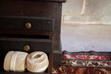 Antique wooden cabinet, dark speckled finish, brass pulls, open drawer with white thread spools.