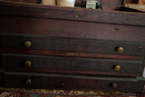 Antique wooden cabinet's dark, aged wood, three drawers, brass knobs, and keyhole.