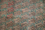 Antique Kerman rug's repeating boteh and Rococo leaves in faded red, jade green, showing foundation wear.
