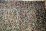 Antique Kerman rug's worn hand-knotted pile, repeating boteh, Rococo leaves, jade green, and red.
