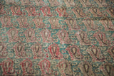 Antique Kerman rug close-up: raspberry botehs and jade scrolling motifs with visible foundation.