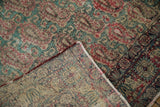 Antique Kerman rug with folded corner revealing pile wear, visible foundation, and tattered edges.