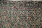 Antique Kerman rug: worn pile, visible foundation, botehs, scrolling leaves, jade green hues.