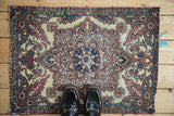 Overhead view of a worn antique Kerman mat, with shoes shown to provide a sense of scale.