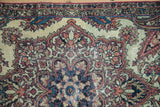 A detailed view of the boteh paisley corner spandrel and trefoil finial on an antique Kerman rug mat.