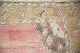 Distressed Kars carpet corner shows raspberry field, dusty gold Rococo border, and fringe.