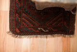 Balouch tribal rug end: deep red, mallard green geometric patterns and textured fringe.