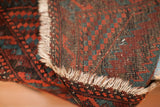 Close-up of the tribal Balouch rug's worn mallard green and rust geometric pattern with tattered fringe.
