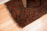 Balouch rug corner shows tattered fringe, deep red and mallard green geometric design.