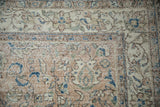 Close-up of distressed Oushak carpet showing faded floral vinery with sapphire blue and sand tones.