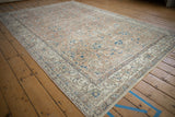 Distressed vintage Oushak rug corner showcasing faded floral vinery and wear to pile.