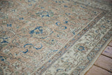 Distressed beige Oushak carpet displaying sapphire blue floral vinery and patterned border.