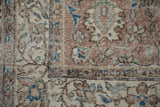 Distressed Oushak carpet close-up, showcasing faded floral vinery in beige, mauve, and sapphire blue.