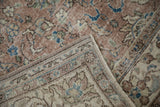 Folded corner of distressed Oushak rug, revealing faded mauve, blue floral vinery, and worn pile.