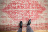 Distressed vintage Oushak rug showing pink raspberry red, ivory hues, and exposed foundation.