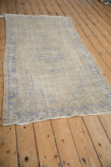 Distressed Oushak rug featuring faded pale blue pattern on an antique ivory field with even wear.