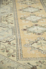 Distressed vintage Melas carpet detail, softened ochre, beige, brown floral patterns, visible wear.