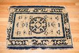 Tattered Early Peking rug fragment showcasing bold ivory field, blue medallion, and pearl border.