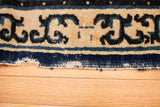 Tattered edge revealing foundation and dark blue pearl border of an early Peking rug fragment.