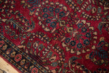 Angled close-up of the dense cherry red pile and floral vines of a vintage Sarouk rug.