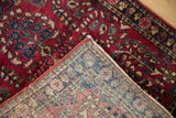 The hand-knotted construction and secured side cord of a vintage cherry red Persian Sarouk rug.