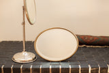 Beveled oval mirror with aged gold frame and polished silver standing mirror base.